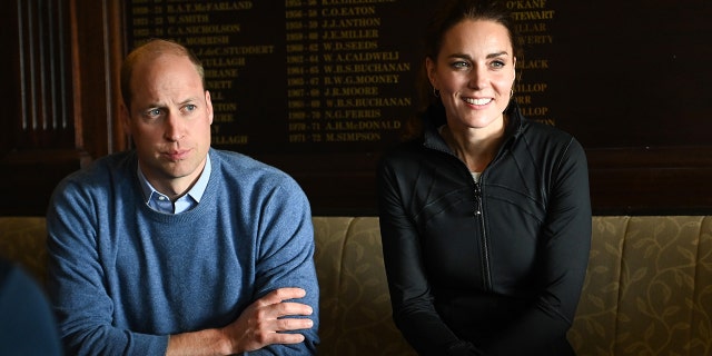 Prince William in a baby blue swearter sitting next to Kate Middleton in a hunter green jacket