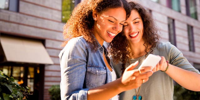 Two women smile as they look at a phone