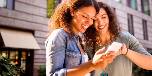 Two women smile as they look at a phone