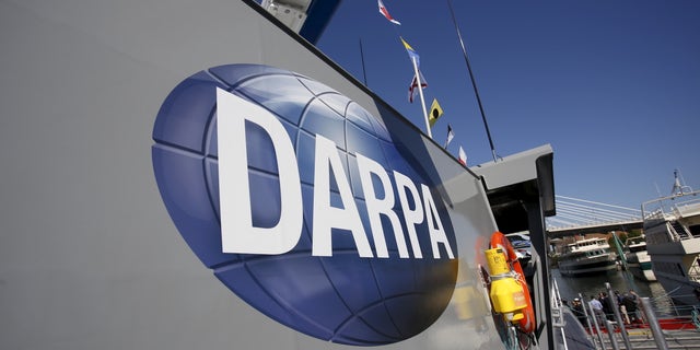 Pentagon announces competition to develop new AI programs, plug holes in national cyber defense DARPA logo on autonomous ship hull