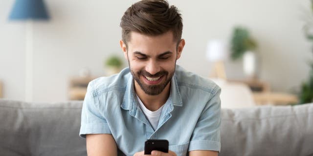 Man smiles as he works on his phone