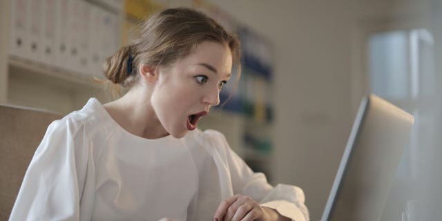 Woman looking at her laptop shocked at finding out that she has been scammed.