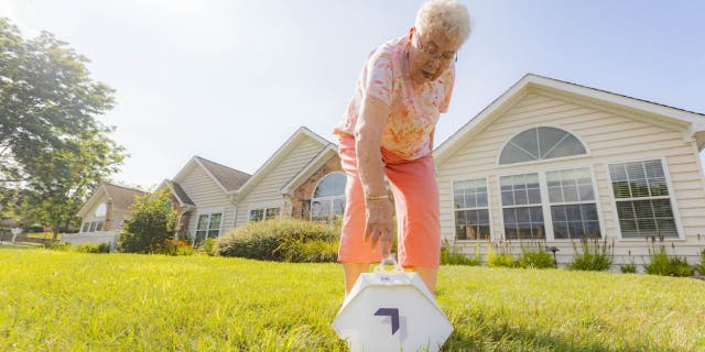 Susie is bending down to pick up her Wing delivery service order in her front yard