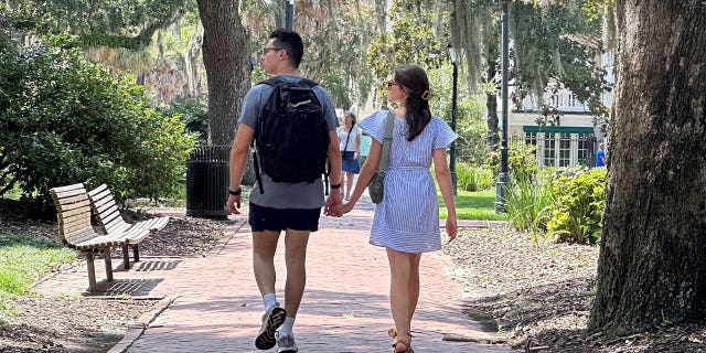 couple holds hands walking through park