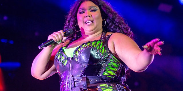 Lizzo in a neon green top with a black bodysuit over it sings on stage in Denmark