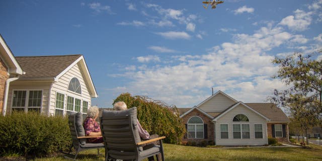 Susie and Paul sitting in chairs outside as a drone in the sky brings them their order