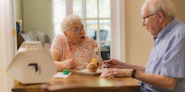 Susie and Paul talking and eating food at their kitchen table from Wing