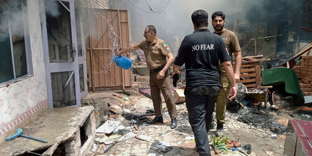 A Pakistani police officer pours water on a burning house