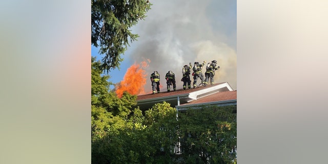 firefighters on roof of building with flames