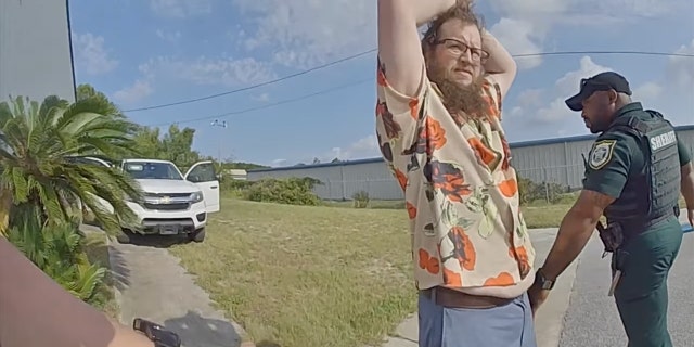 Burglar raising his arms over his head as he is detained by police.