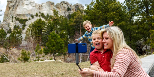 A mother poses for a selfie with her two sons with Mt. Rushmore in the background