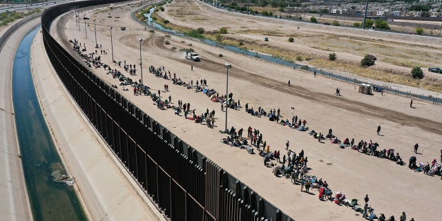 Migrants wait along border wall