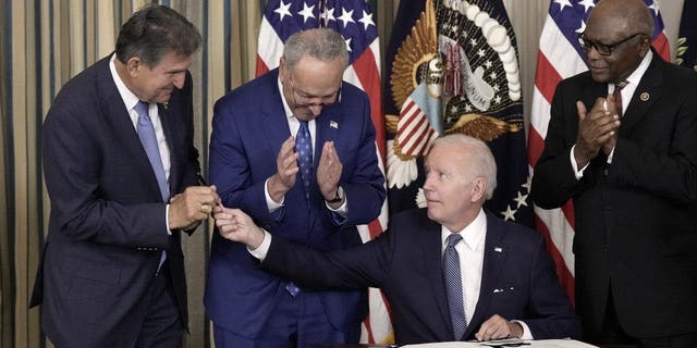 President Joe Biden (C) gives Sen. Joe Manchin (D-WV) (L) the pen