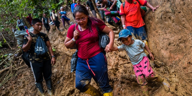Ecuadorian migrants climb down a muddy hillside trail in Darién Gap, Colombia