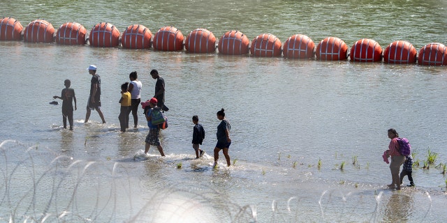 Migrants walk near the floating barrier in the Rio Grande