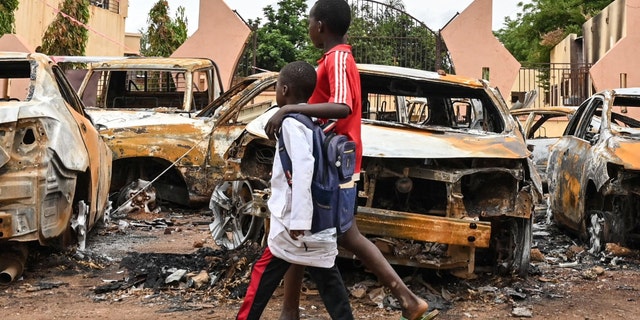 burned out cars on street as children walk by