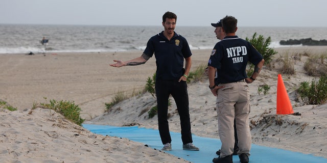NYPD officers stand on Rockaway Beach after shark attack