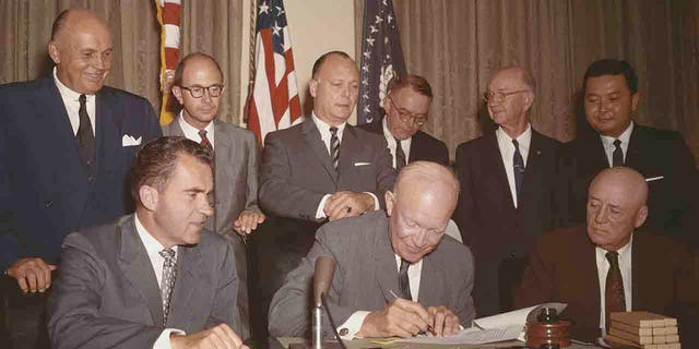 Dwight Eisenhower signing paper as Richard Nixon, and others look on