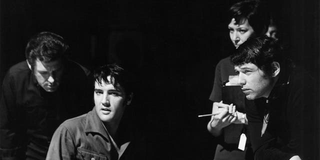 Elvis Presley looking away as he suits next to several men on stage