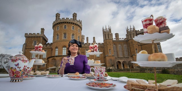 Emma Manners wearing a purple dress with a matching hat having tea outside Belvoir Castle