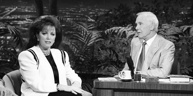 A black and white photo of Jackie Collins being interviewed by Johnny Carson