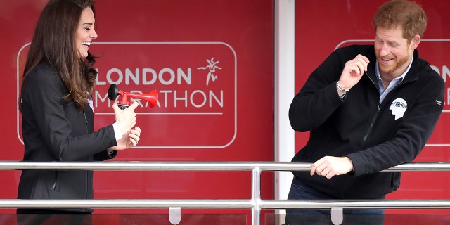 Kate Middleton laughing and blowing a horn in front of a startled Prince Harry