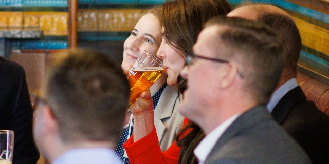 Kate Middleton wearing a red dress drinking a beer