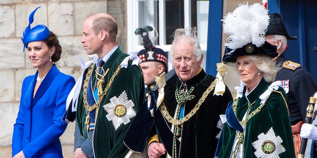 Kate Middleton in a cobalt blue dress and matching hat standing next to Prince William, King Charles and Queen Camilla as they wear formal royal wear