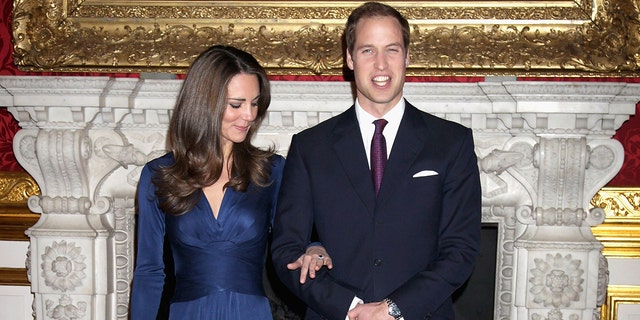 Kate Middleton in a blue wrap dress staring at her engagement in the arm of Prince William