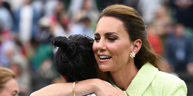 Kate Middleton in a lime green dress hugging a woman on the field