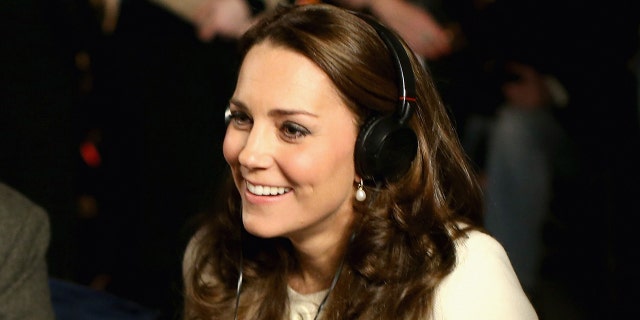 A close-up of Kate Middleton wearing a white sweater and headphones