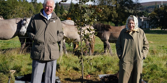 Prince Charles and Queen Elizabeth smiling in matching green outfits in a field