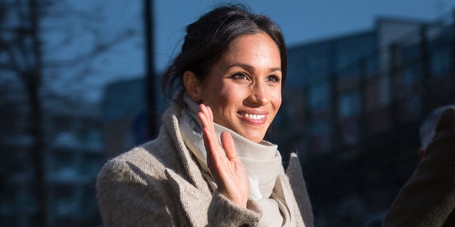 Meghan Markle waving and wearing a beige coat with a matching turtleneck sweater