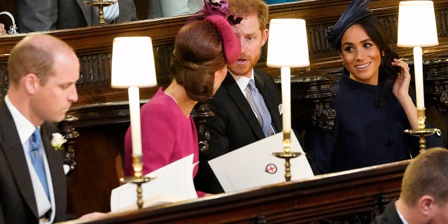 Kate Middleton wearing a pink dress and matching hat chatting with Prince Harry- in a suit and tie