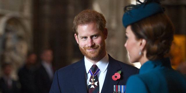 Prince Harry in a suit and tie admiring Kate Middleton in a blue dress with a matching fascinator