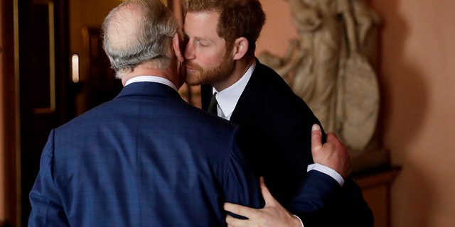 King Charles with his back turned being kissed on the cheek by Prince Harry