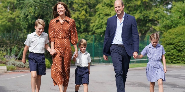 Kate Middleton in a polka dot brown dress walking alongside Prince William and their three children as they wear various shades of blue and white