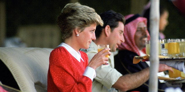 Princess Diana wearing a red and white dress drinking next to Prince Charles
