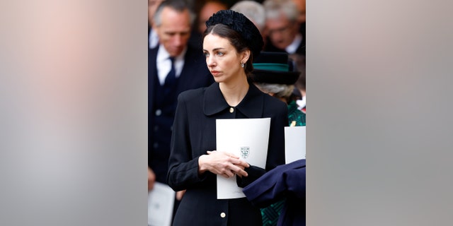 Rose Hanbury wearing a black coat dress and holding a program