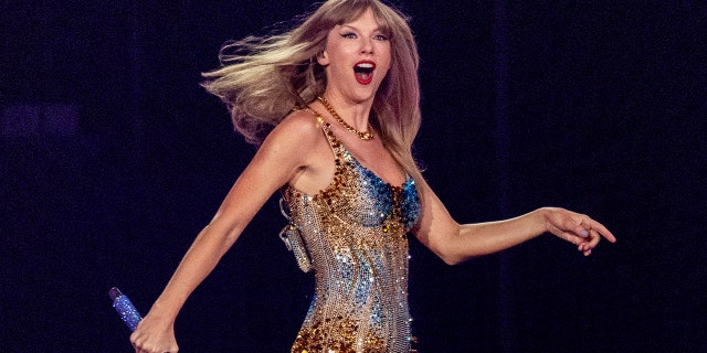 A close-up of Taylor Swift wearing a sparkling costume on stage while she holds a mic