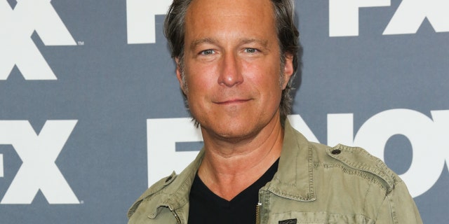 John Corbett smiling and wearing a khaki jacket