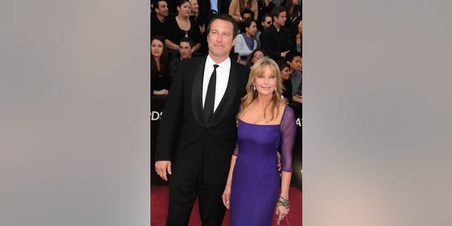 John Corbett on the red carpet next to Bo Derek in a purple dress