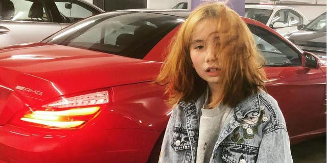Lil tay poses by red sports car wearing denim coat