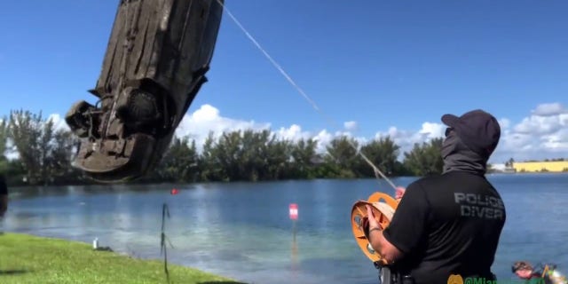 police officer looks on as submerged car removed from lake