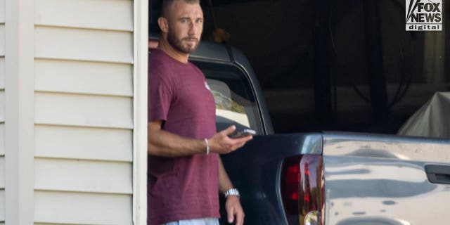 Richard Tobin in blue shorts and and a purple t-shirt looks suspicious as he peeks from the garage