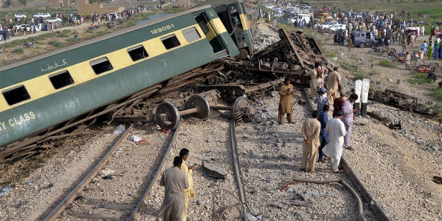 People looking at the derailed train cars in Pakistan