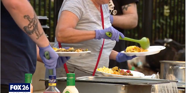 A volunteer can be seen scoops food into a plate outside the Houston Public Library downtown