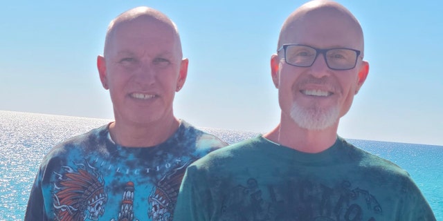 Herbert Swilley and Tim Smith pose together at the waterfront, backlit, wearing T-shirts