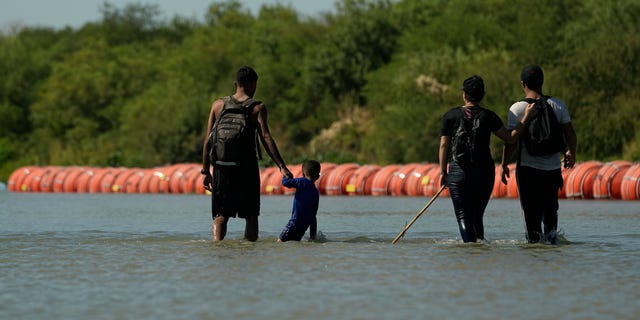 Migrants walk near Texas floating border barrier