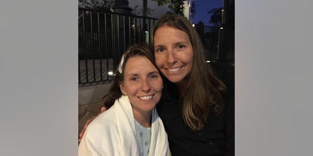 Wendi Lou Lee in a white robe and light blue shirt posing with her twin sister in a black turleneck sweater